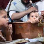 φωτογραφία βάπτισης, ο Δημήτρης μέσα στην κολυμπήθρα. Το χέρι το ιερέα πάνω στο κεφάλι του μικρού.
