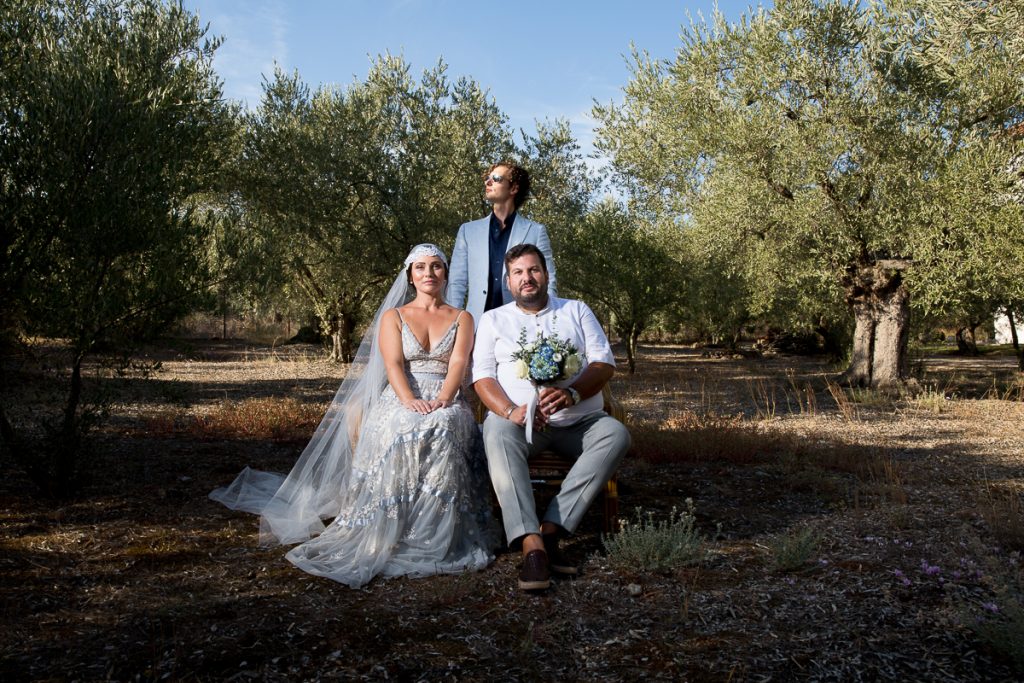 το ζευγάρι και ο κουμπάρος όρθιος φωτογραφίζονται σε έναν ελαιώνα.