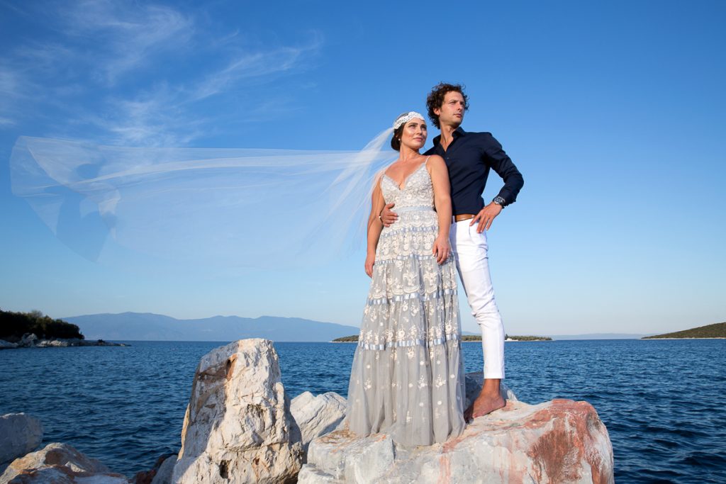 το ζευγάρι είναι ανεβασμένο στα βράχια, το πέπλο της νύφης ανεμίζει.