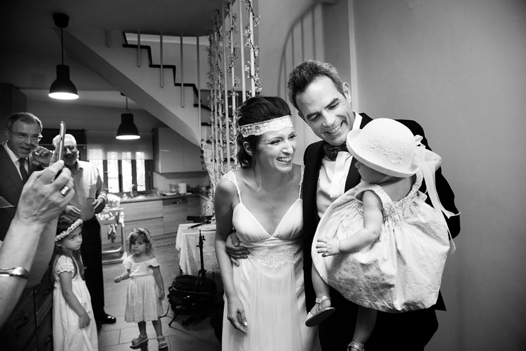 η οικογένεια κρατάει το παιδί τους στην αγκαλιά και χαμογελούν όλο ευτυχία. γάμος και βάπτιση μαζί, ο φωτογράφος γάμου παρουσιάζει μια γαμοβάπτιση στη Θεσσαλονίκη.