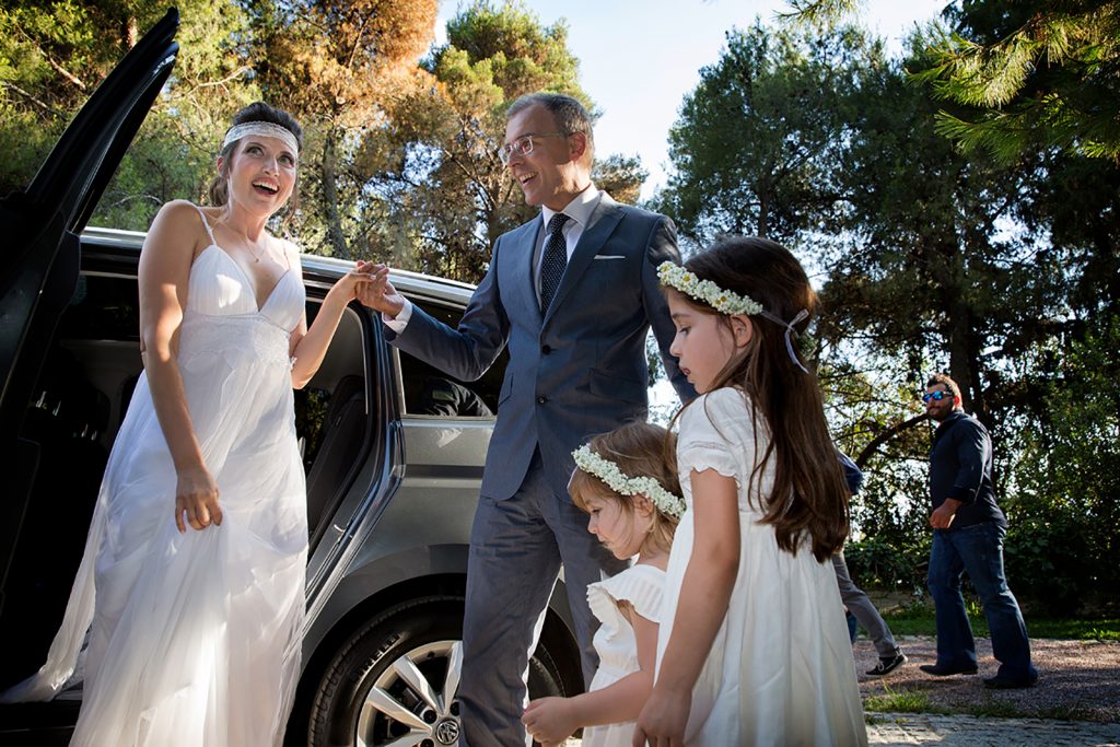 ο κουμπάρος βοηθάει τη νύφη να βγει από το αμάξι, δίπλα ένα παρανυφάκι.