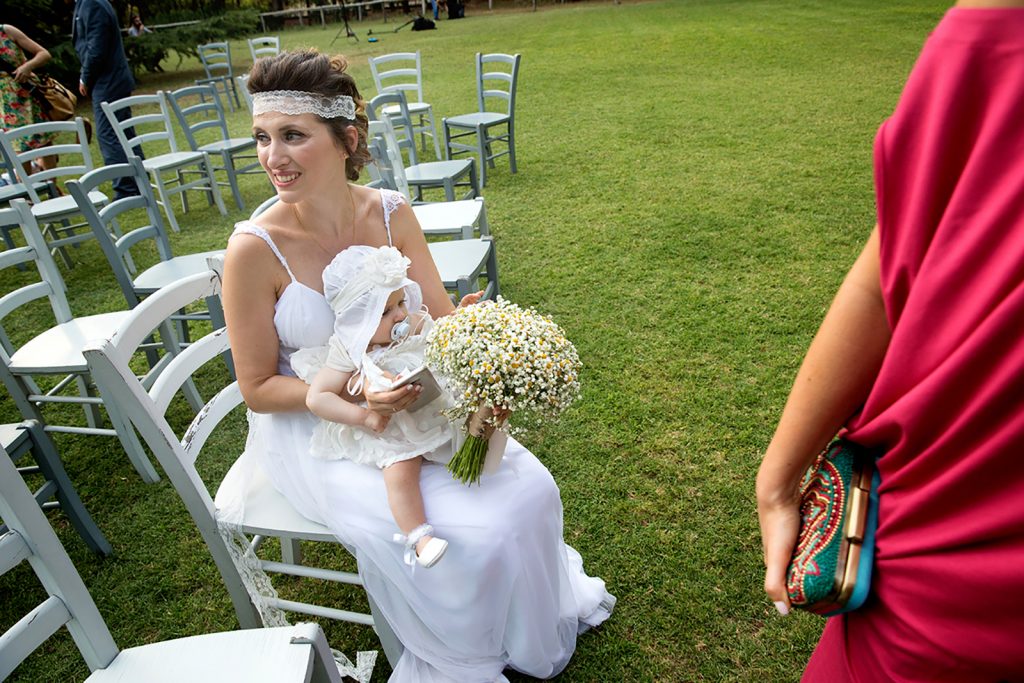 η μητέρα με την κόρη στην αγκαλιά, δίπλα τους ένα κόκκινο φόρεμα, γάμος και βάπτιση μαζί, ο φωτογράφος γάμου παρουσιάζει μια γάμο βάπτιση στη Θεσσαλονίκη.