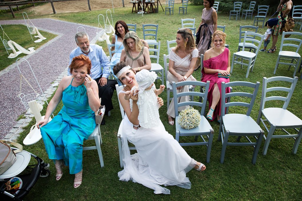 η γιαγιά μιλάει στο κινητό, η μητέρα με την κόρη στην αγκαλιά της και φίλοι γύρω τους, κάθονται σε ξύλινες καρέκλες