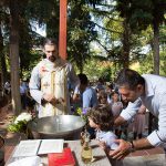 ο νονός μιλάει σε έναν μικρό , ο ιερές ψέλνει μπροστά από την κολυμπήθρα.