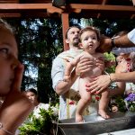 οι νονοί λαδώνουν το μικρό, η αδελφή του δίπλα με το δάκτυλο στο στόμα.