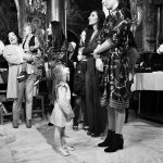 ασπρόμαυρη φωτογραφία από τη βάπτιση. μια μικρή κυρία κοιτάει μια μεγάλη κυρία επίμονα ενώ μια άλλη χοροπηδάει από ευρυχία. Τι πράγματα συμβαίνουν σε μια εκκλησία.
