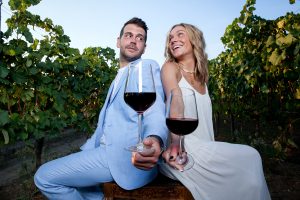 νιόπαντρο ζευγάρι προεκτείνουν τα χέρια τους κρατώντας ποτήρι κόκκινο κρασί.
